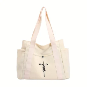 Bolso tote grande de lona crema con bolsillos laterales y una cruz con la palabra Jesus